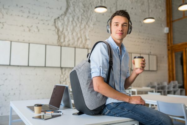 pretty young handsome man sitting on table in headphones with backpack