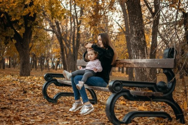 Young female woman babysitter and toddler baby girl walk in autumn park. Happy family mom and