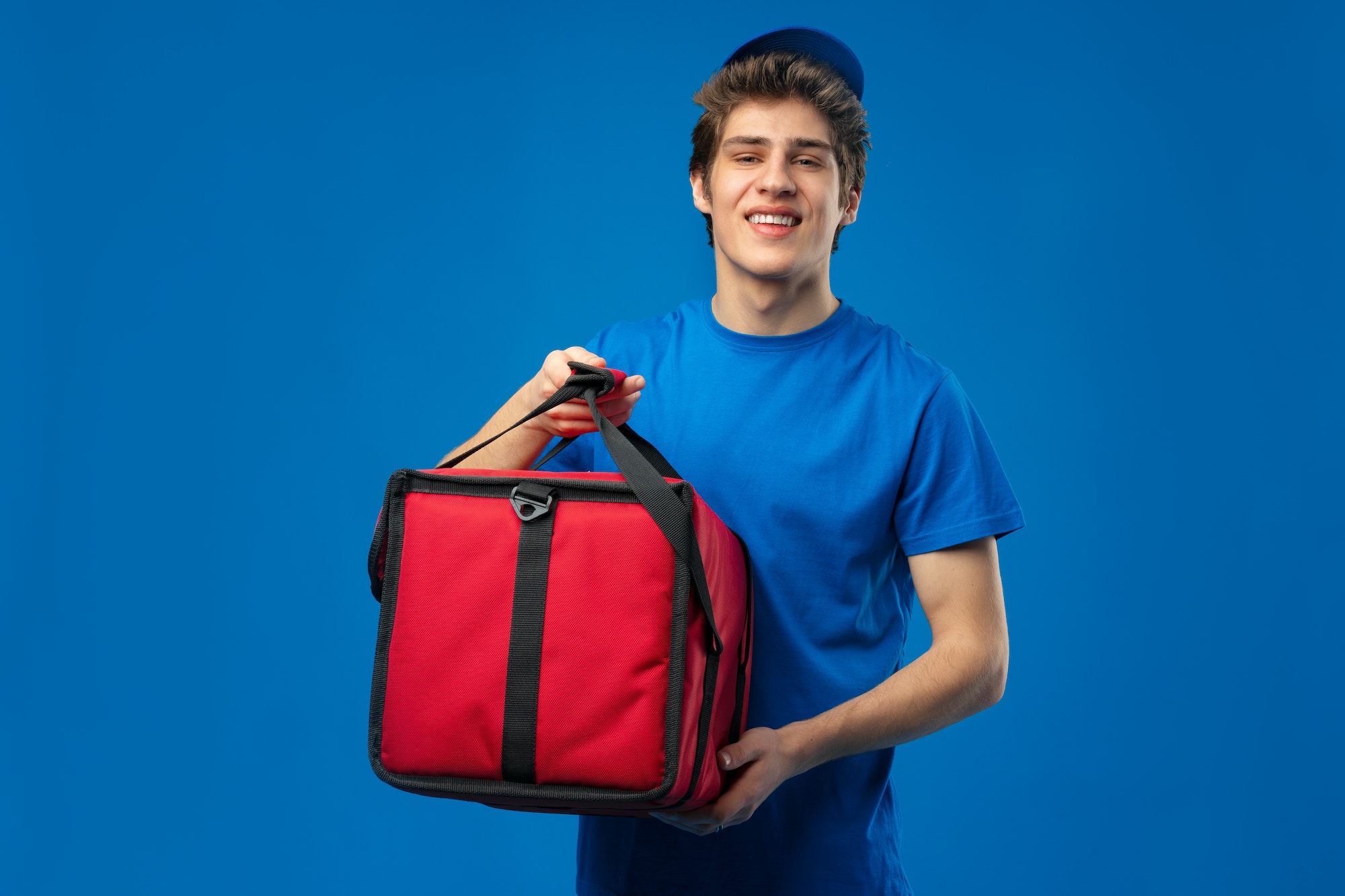 Young courier with thermo bag on blue background